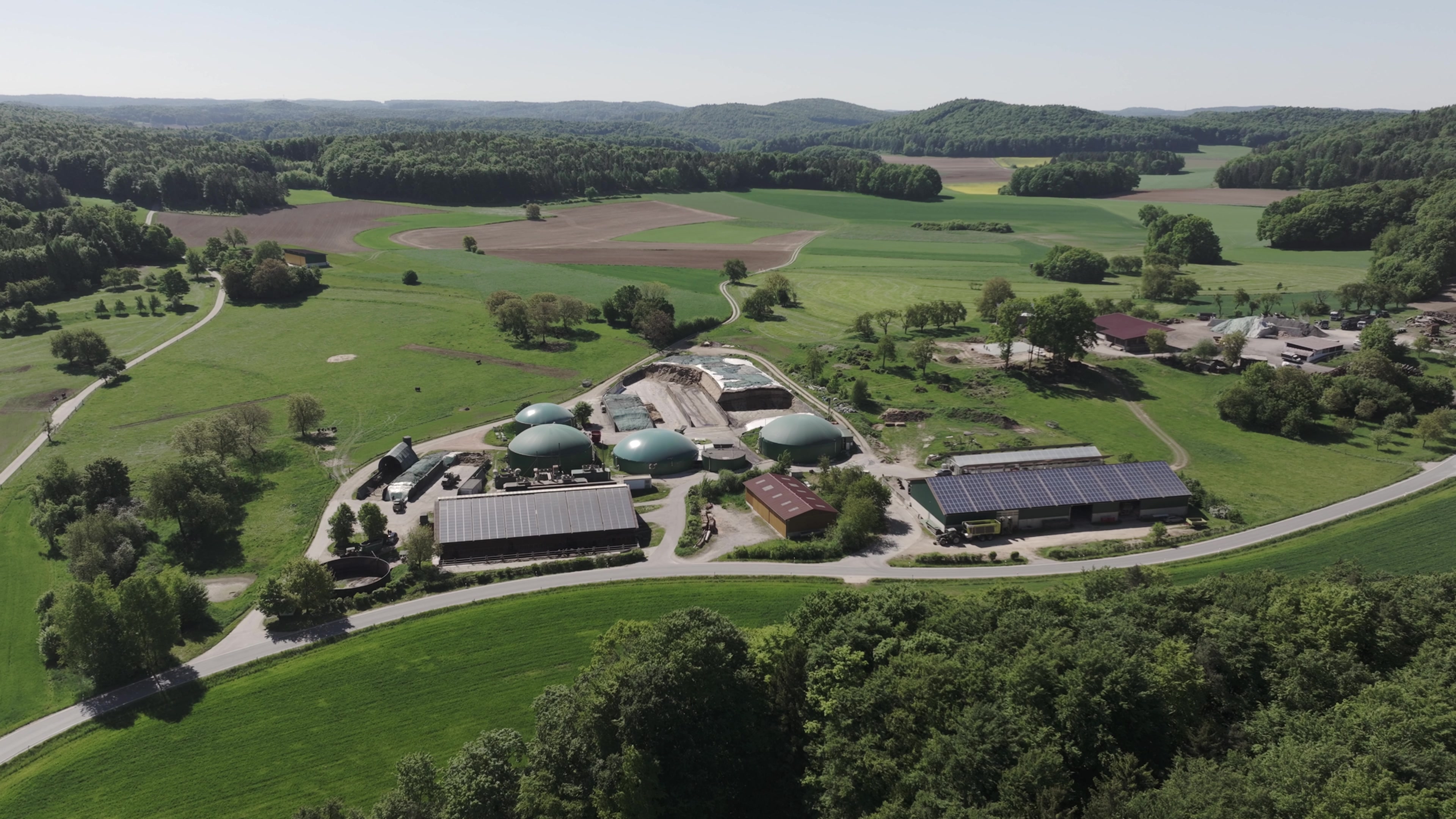 Luftaufnahme unserer Biogasanlage am Wiesenthof mit grünen Behälterdächern, Trocknungshalle und Photovoltaik